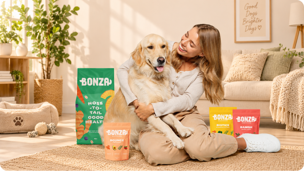 A woman hugging a golden retriever on a living-room rug, surrounded by Bonza food and supplement bags